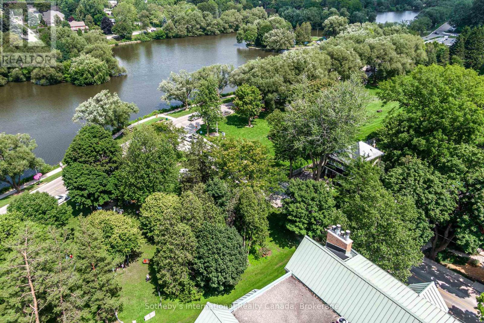 Aerial view of a tree-lined river beside parkland and nearby rooftops.