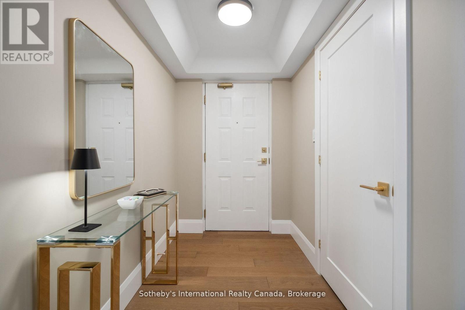 Condo entry hall with wood flooring, a gold-framed mirror, and a glass console table.