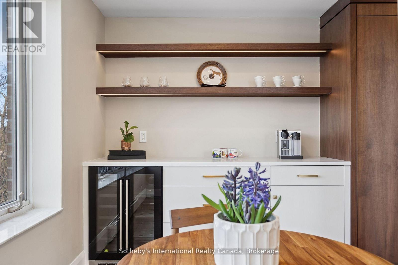 Beverage station with dark wood shelves, a glass-front wine fridge, and a coffee machine beside a dining table.