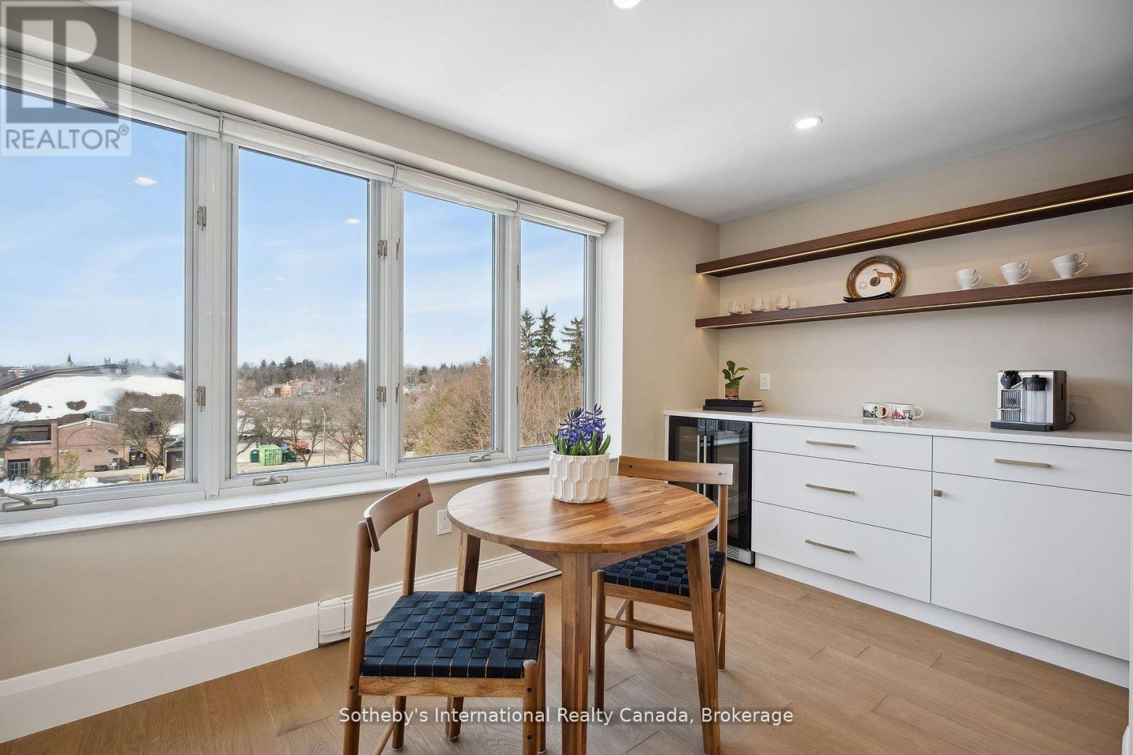 Dining area with a round wooden table and large windows overlooking a snow-dusted town.