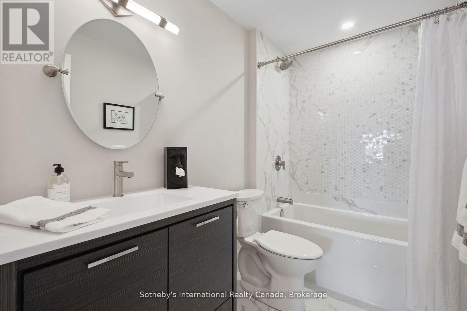 Modern bathroom with dark wood vanity, oval mirror, and white hexagonal tile around the bathtub.