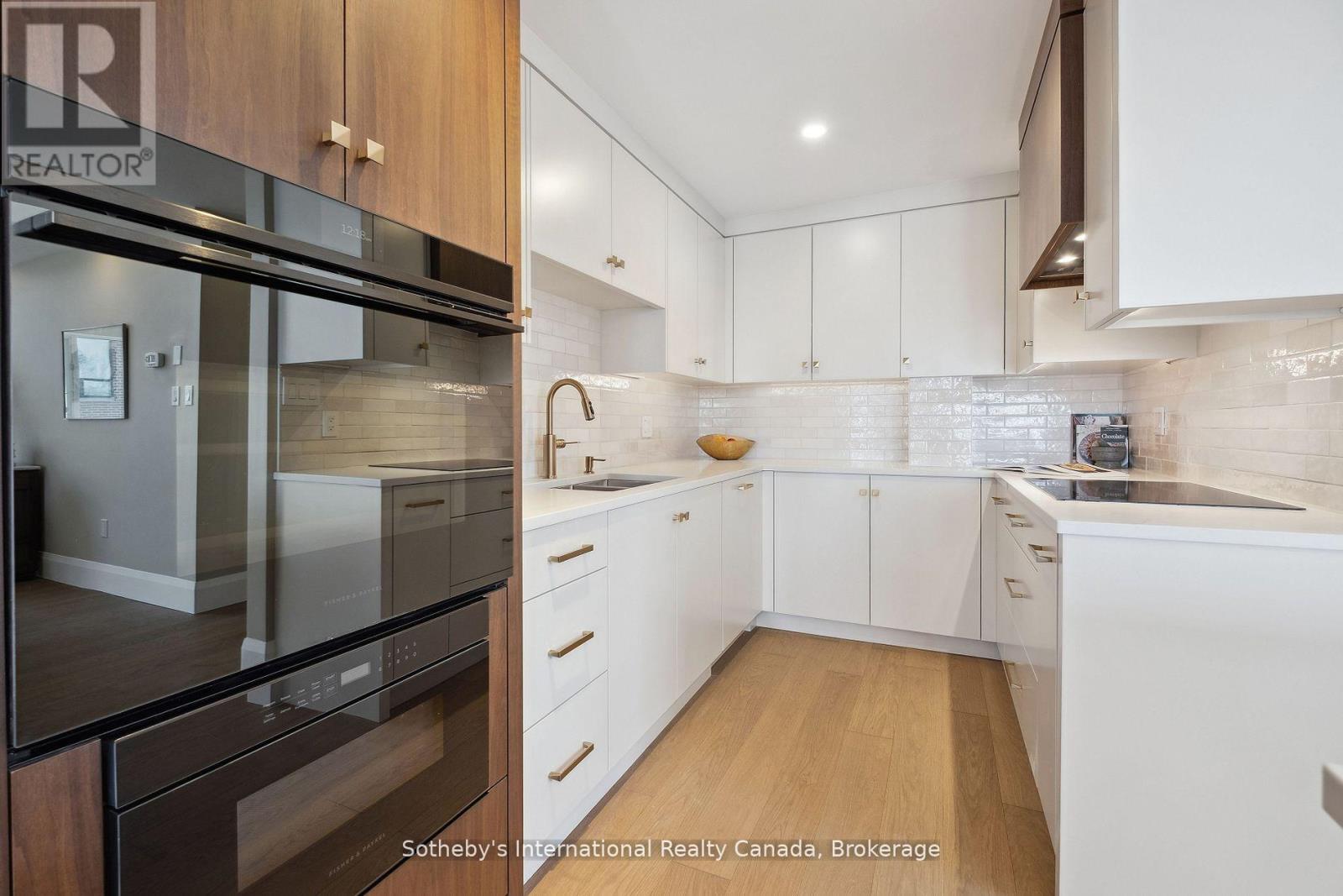 Modern kitchen with white cabinetry, warm wood accents, glossy tile backsplash, and built-in double oven.