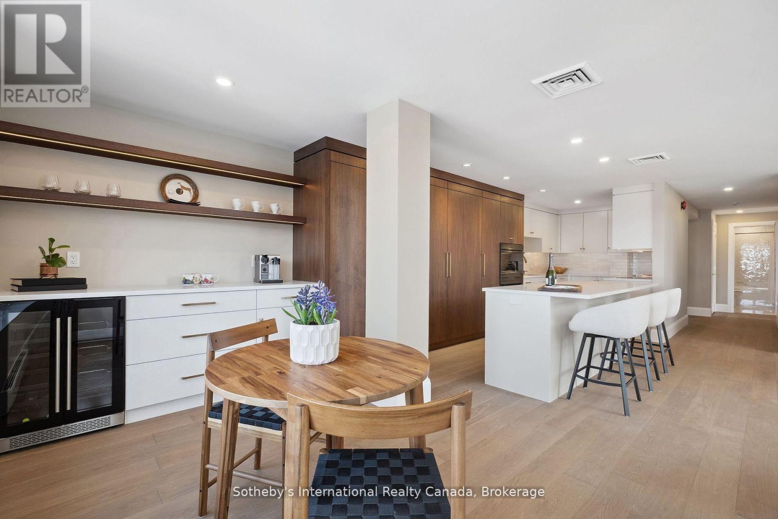 Modern kitchen with dark wood cabinetry, white island, bar stools, and a round dining table.