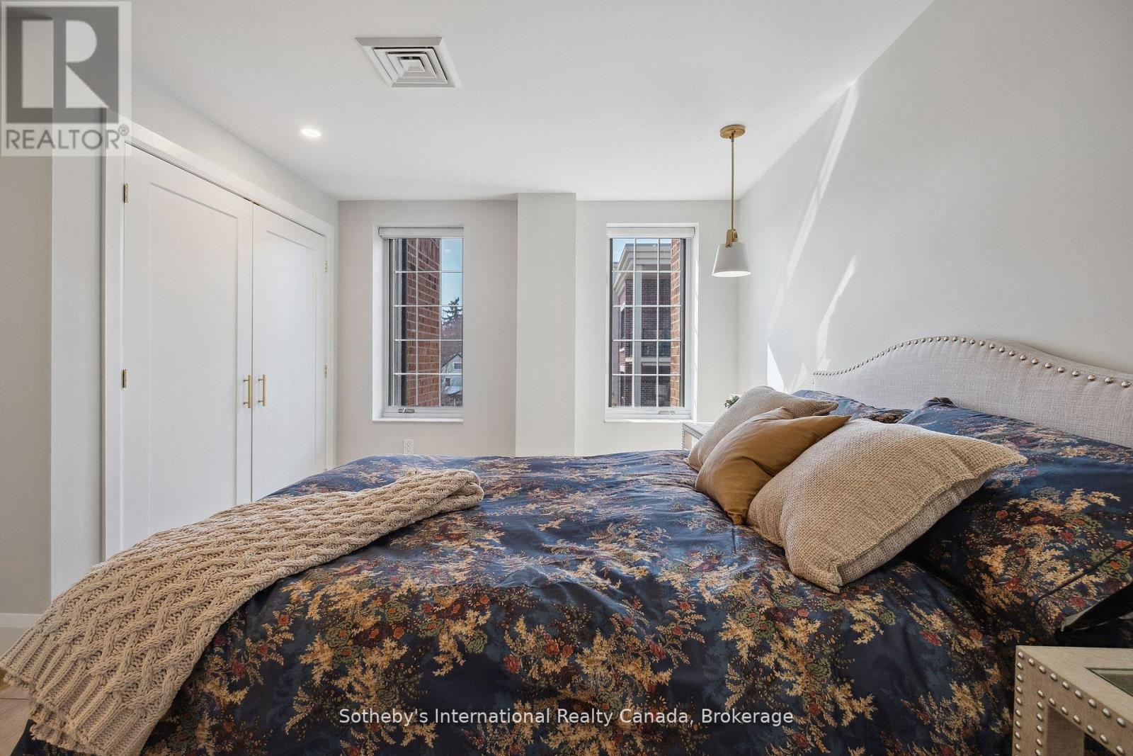 Furnished bedroom with a floral bedspread, knitted throw, and two tall windows.