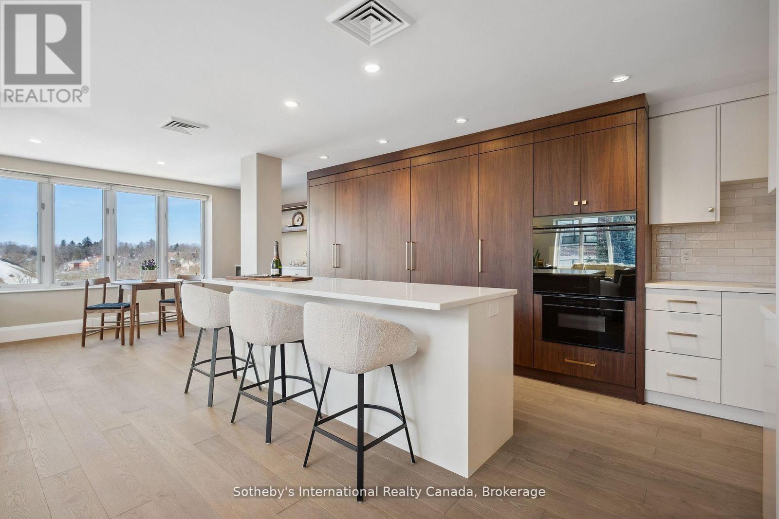 Modern condo kitchen with a white island, dark wood cabinetry, and a dining nook by large windows.
