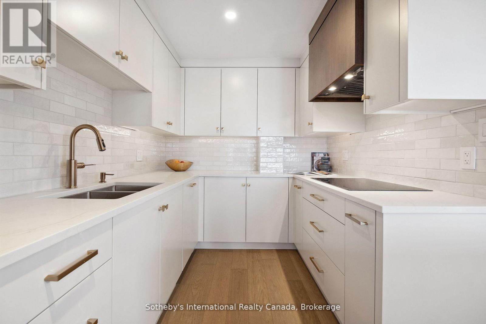 Modern white kitchen with brass hardware, glossy tile backsplash, and wood flooring.