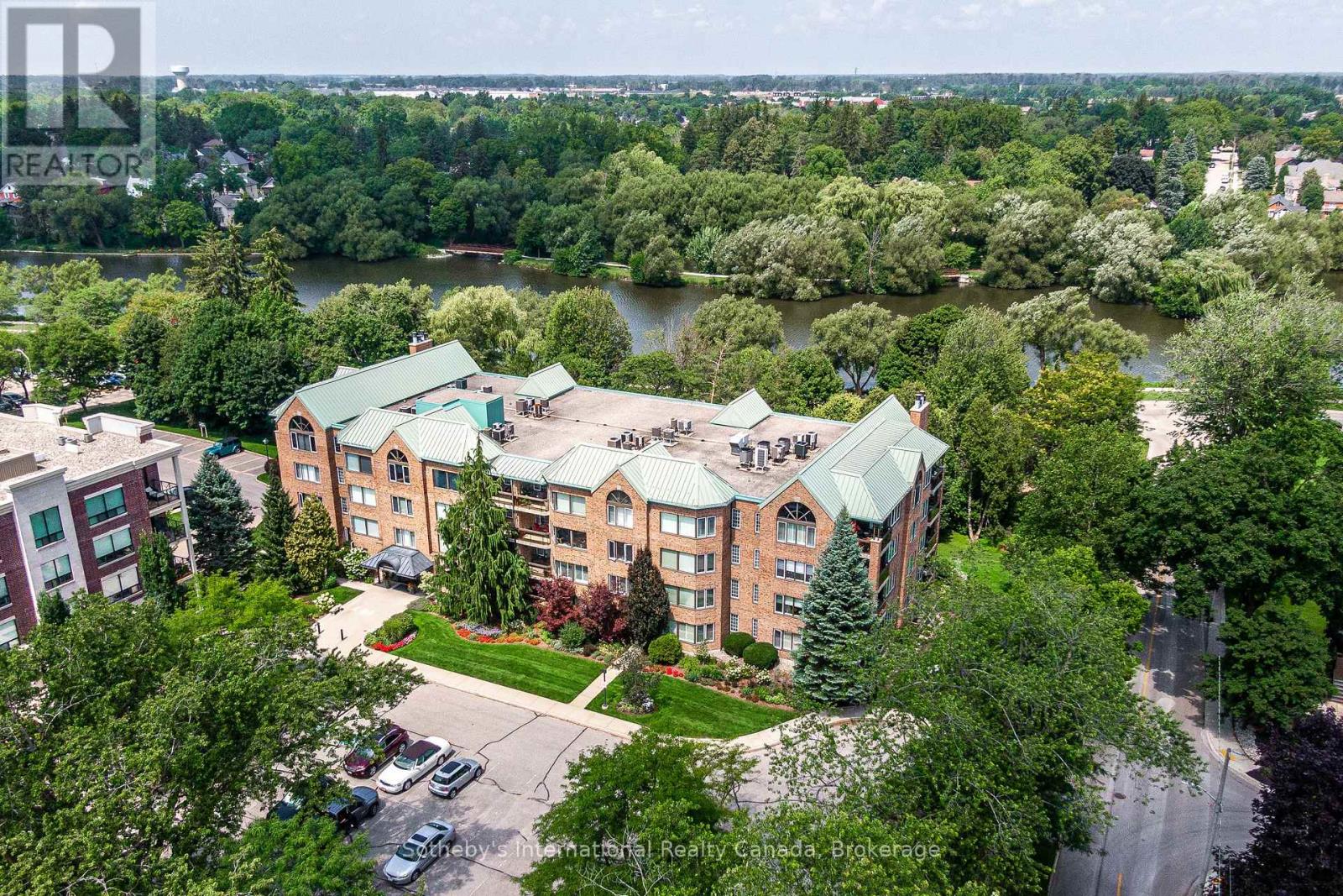 Brick condominium building with green roofs beside a tree-lined river in Stratford.
