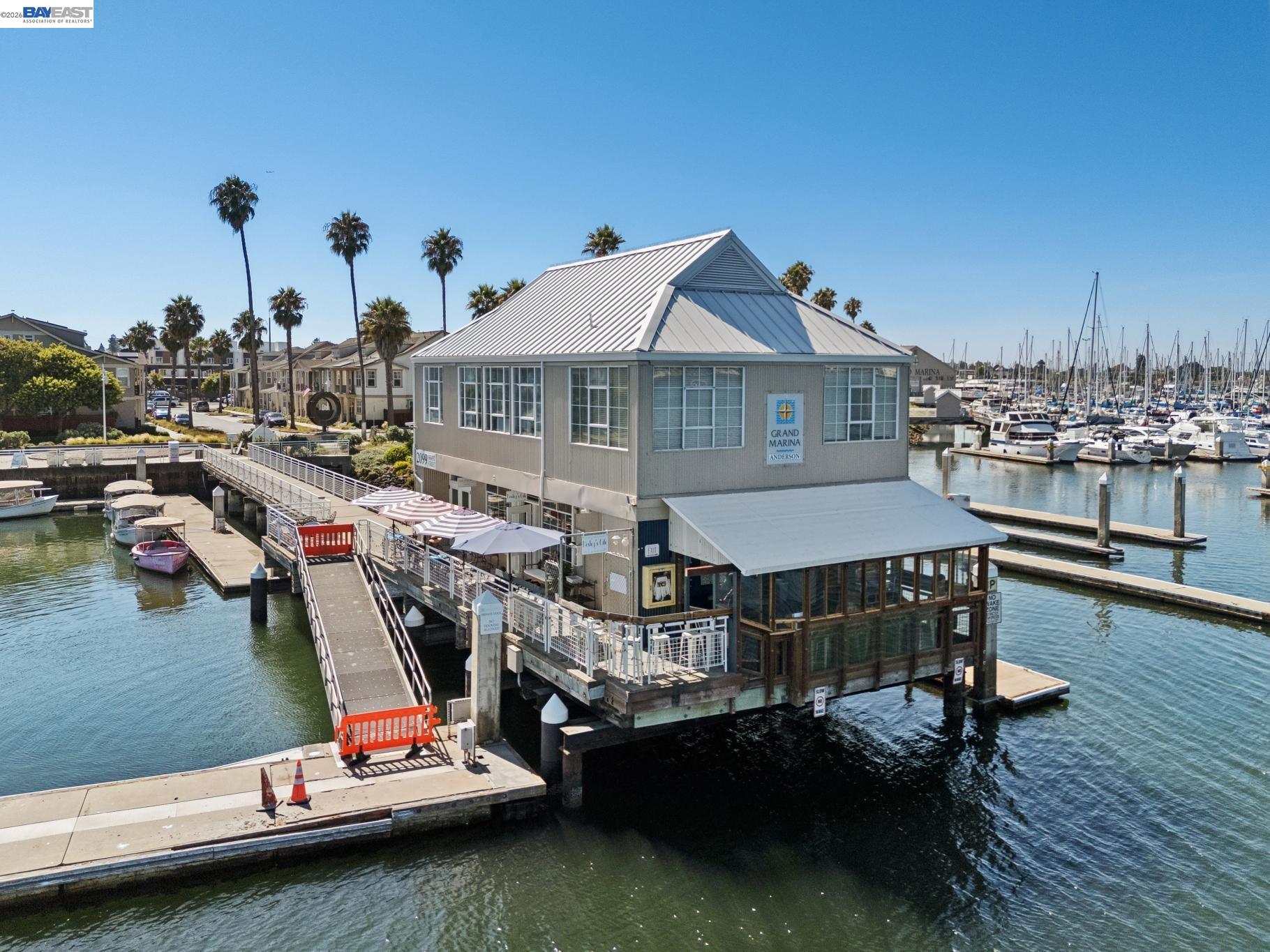 Marina building over the water, with docked boats and palm trees in the background.