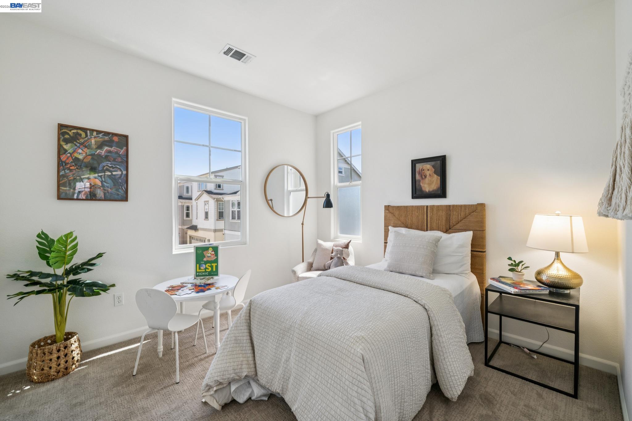 Furnished bedroom with a woven-headboard bed, two tall windows, and a small children's table.
