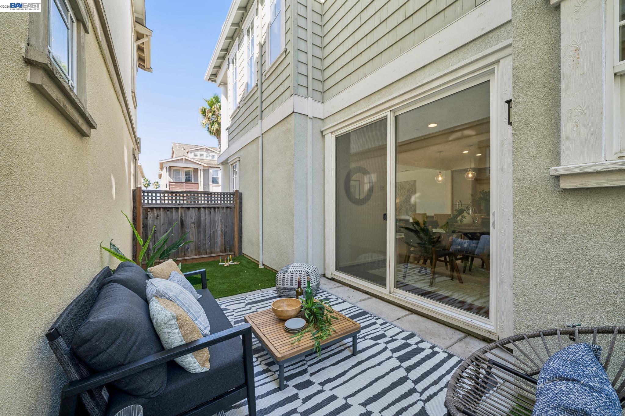 Outdoor patio with cushioned seating, patterned rug, artificial turf, and sliding glass doors.