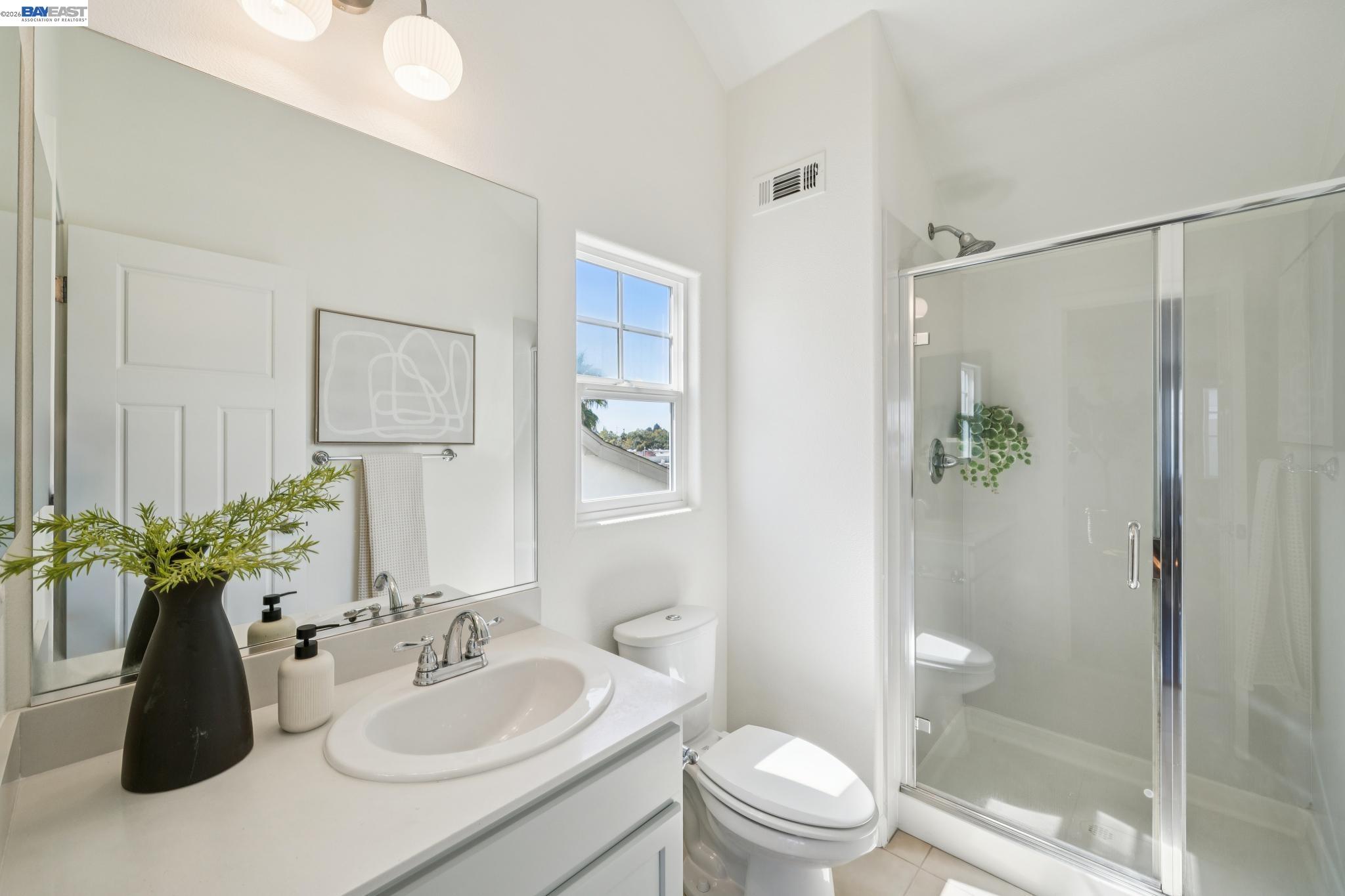 Bright bathroom with a white vanity, window, toilet, and glass-enclosed shower.