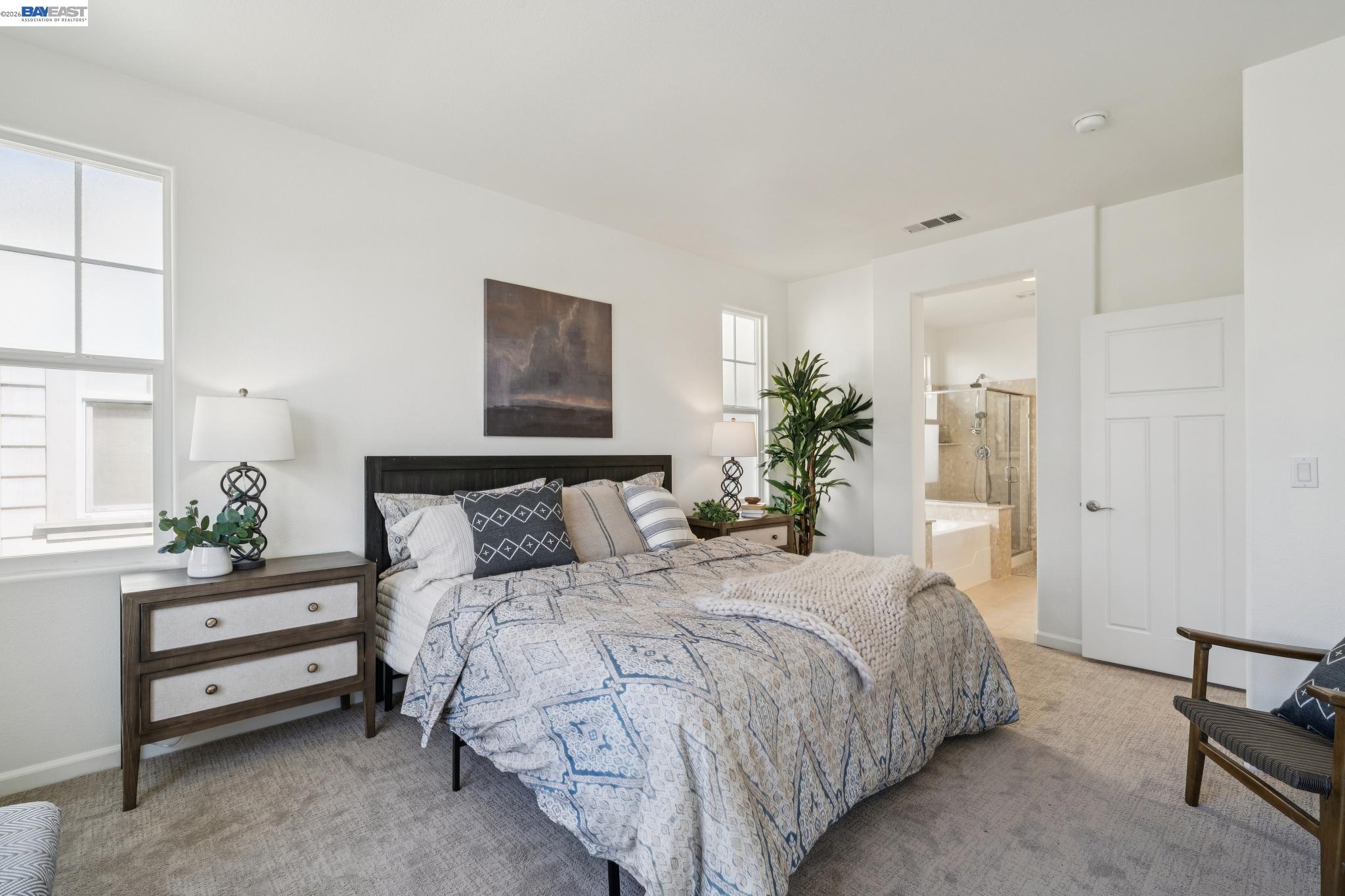Furnished bedroom with patterned bedding, tall windows, and an open doorway to the en-suite bathroom.