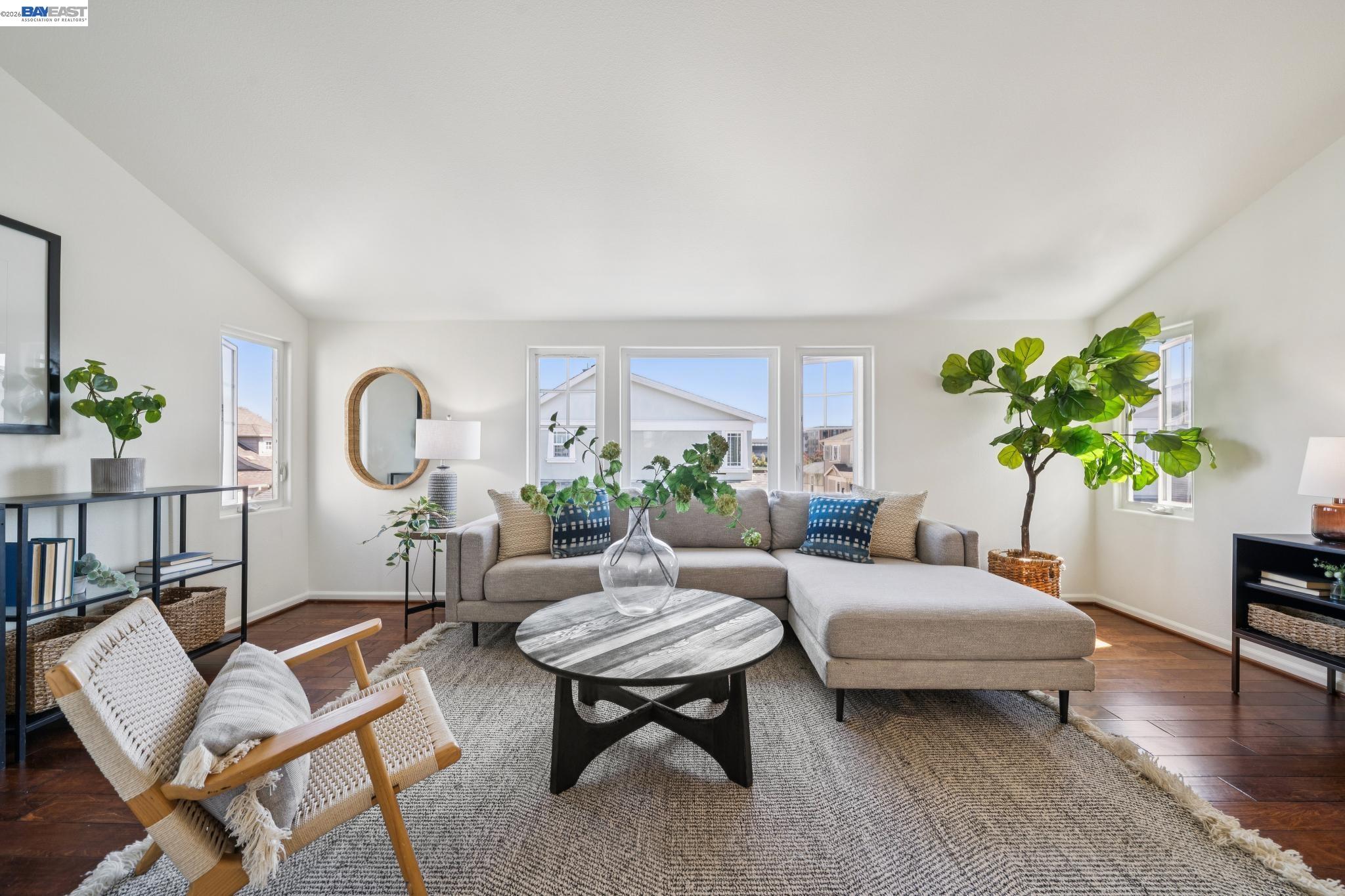 Staged living room with a gray sectional, woven chair, round coffee table, and windows.