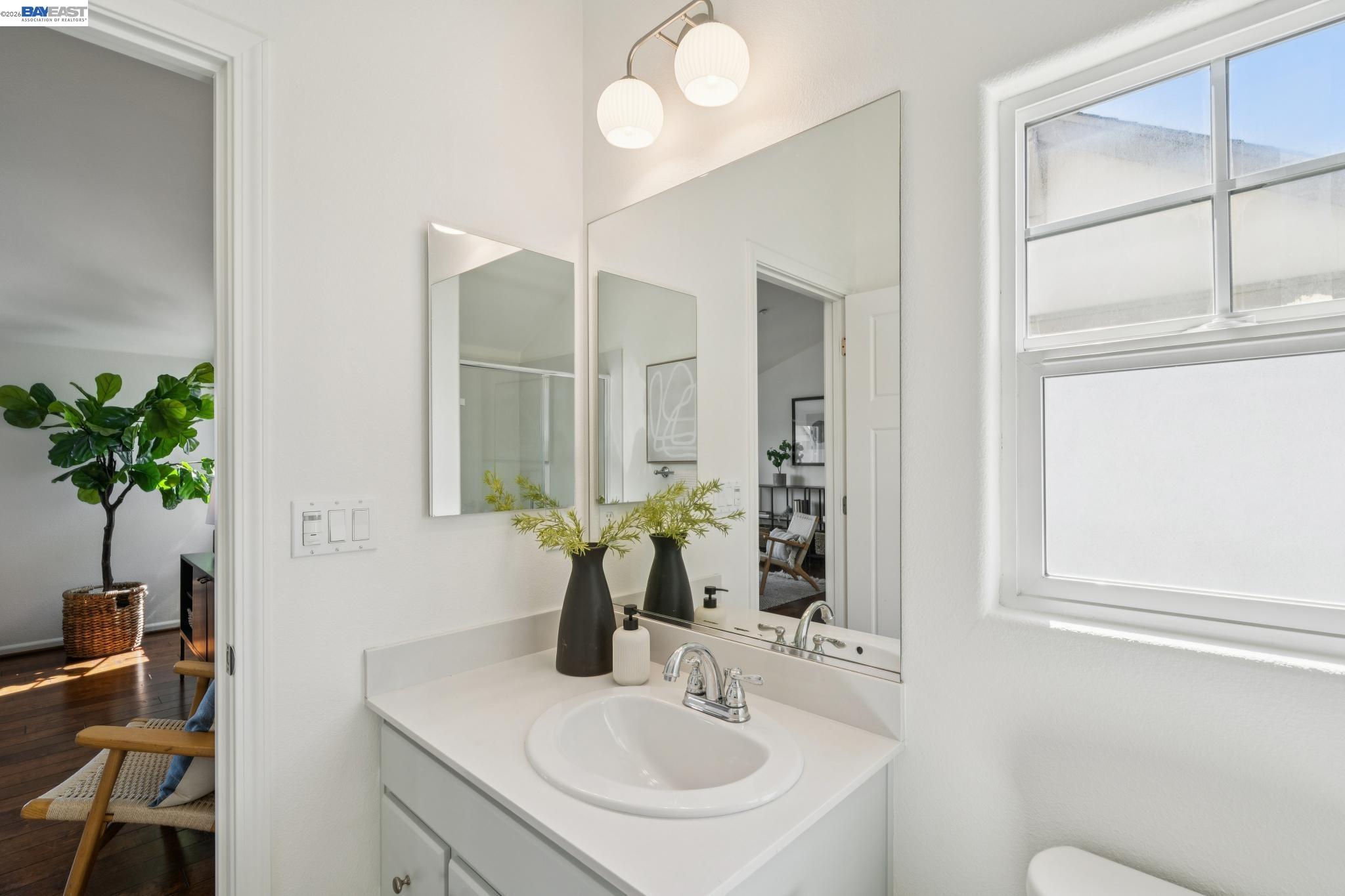 Bathroom vanity with a large mirror, two-globe light, and window beside a furnished sitting area.