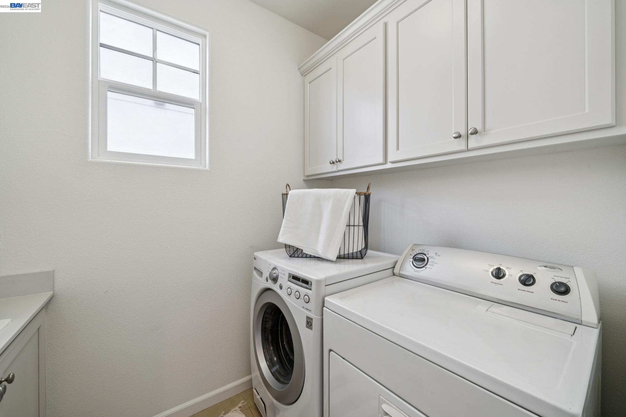 Laundry room with white cabinets, a high window, and side-by-side washer and dryer.