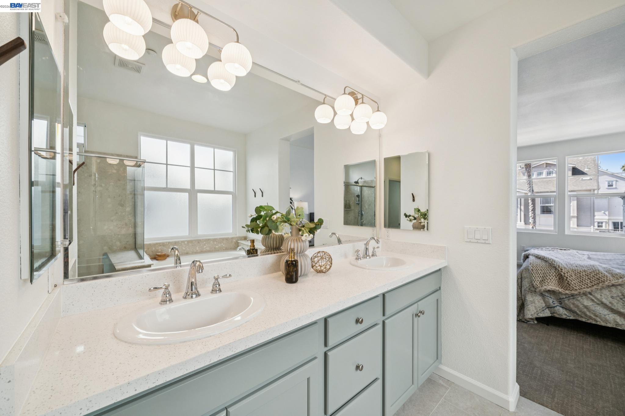 Bathroom with a double-sink vanity, globe pendant lights, and an adjoining bedroom visible through the doorway.