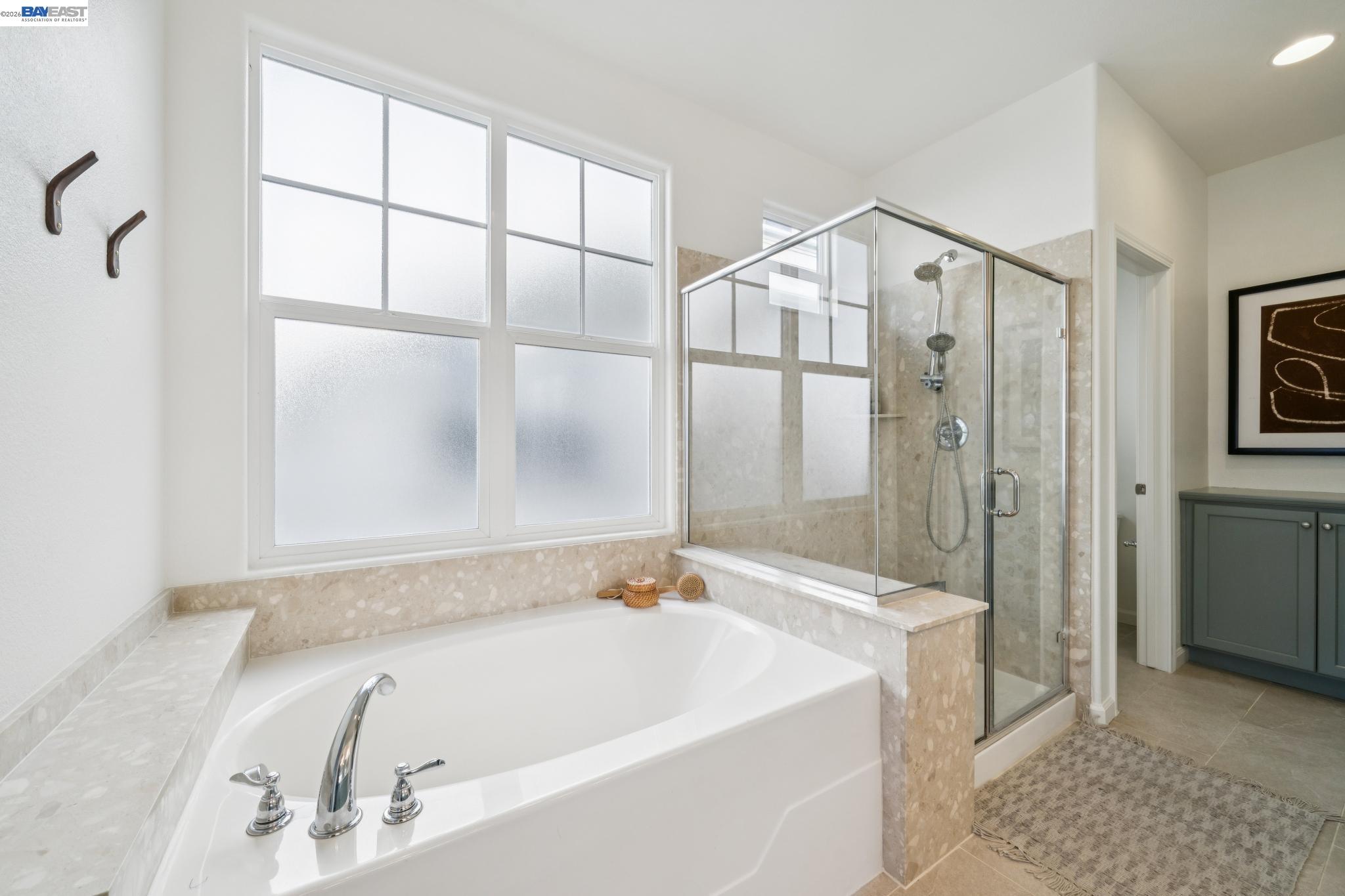 Bathroom with a soaking tub beneath frosted windows and a glass-enclosed shower.