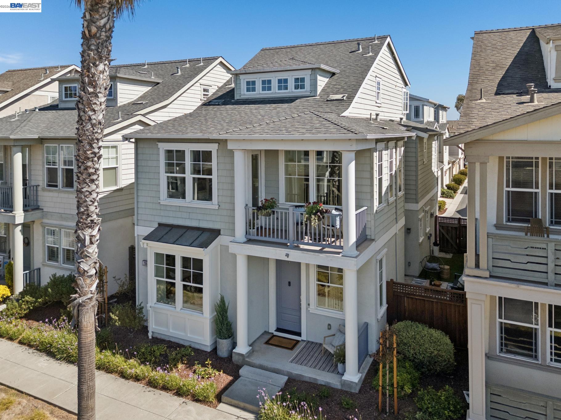 Light gray multi-story home with a covered balcony and porch, seen from above the front garden.