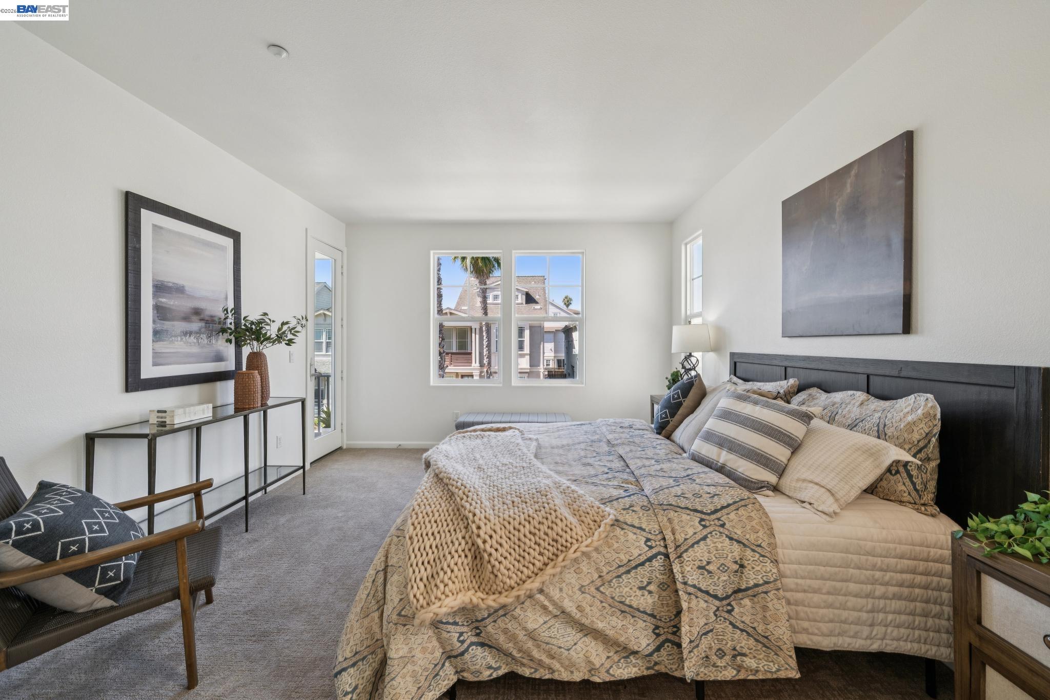 Staged bedroom with patterned bedding, dark wood headboard, and windows overlooking neighboring homes.
