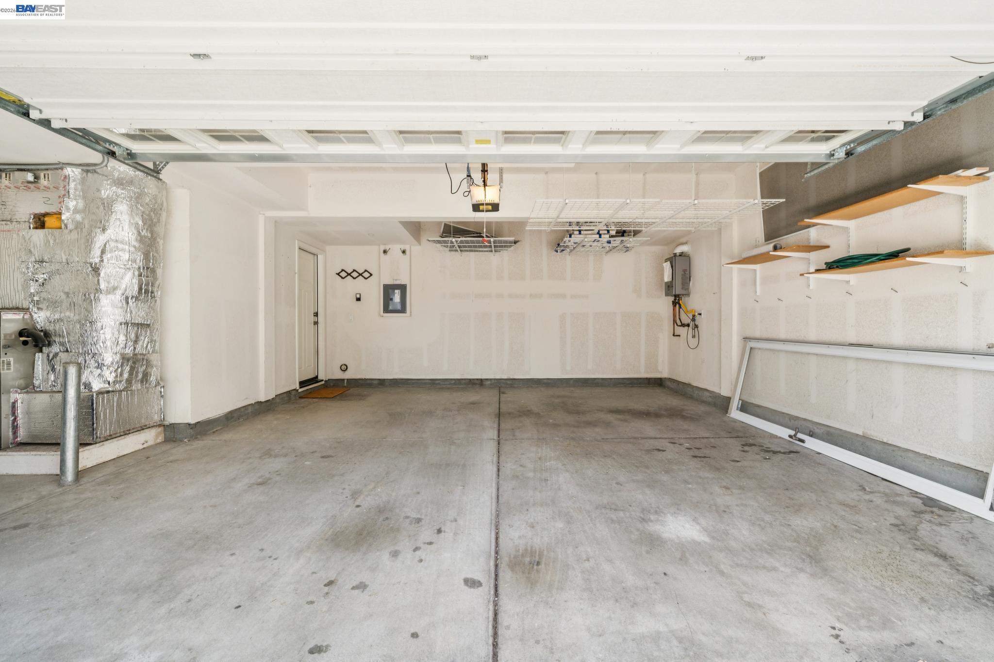 Empty garage with a raised overhead door, concrete floor, and wall-mounted storage shelves.