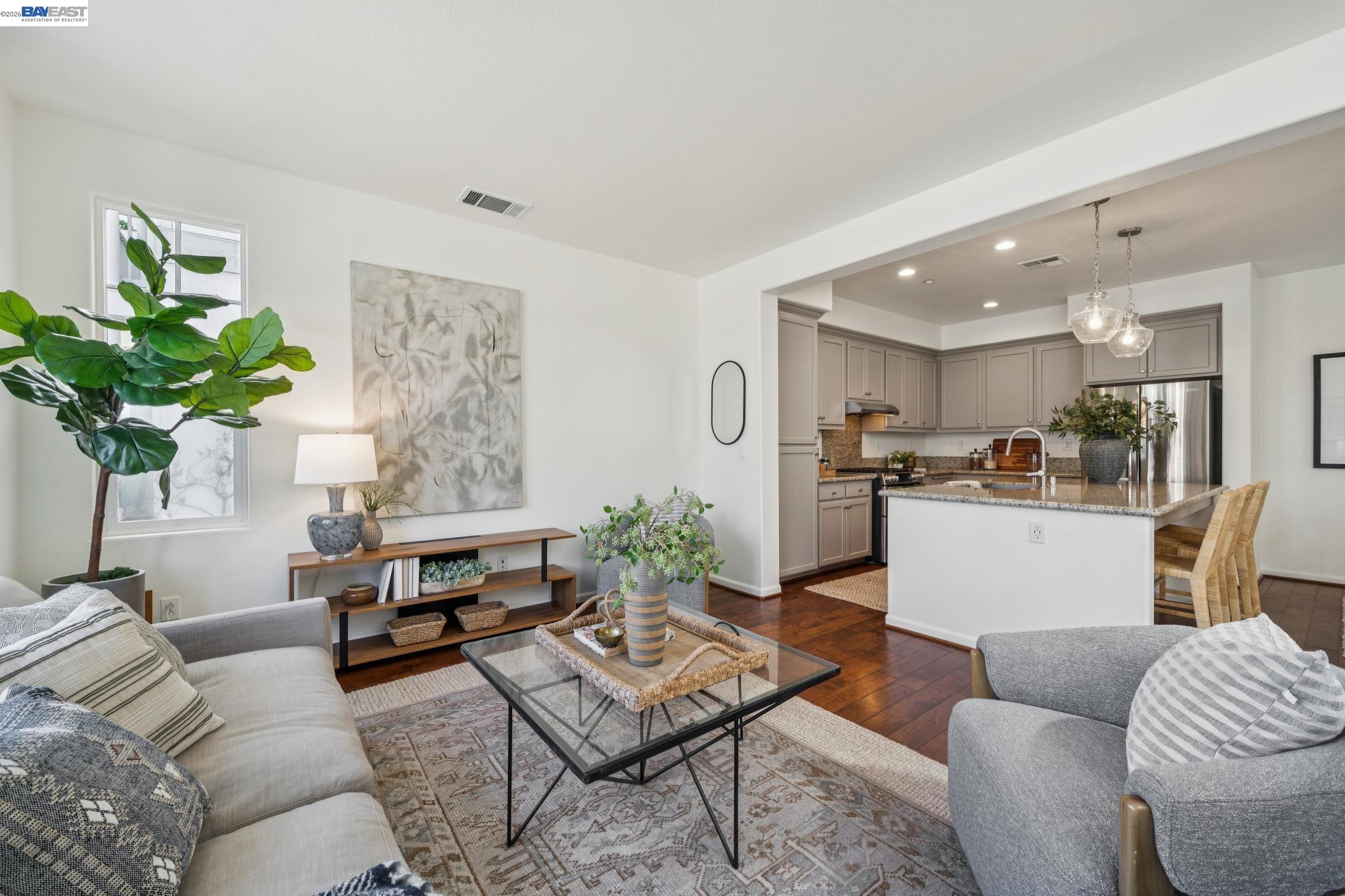 Staged living room opens to a kitchen with a granite island and taupe cabinetry.
