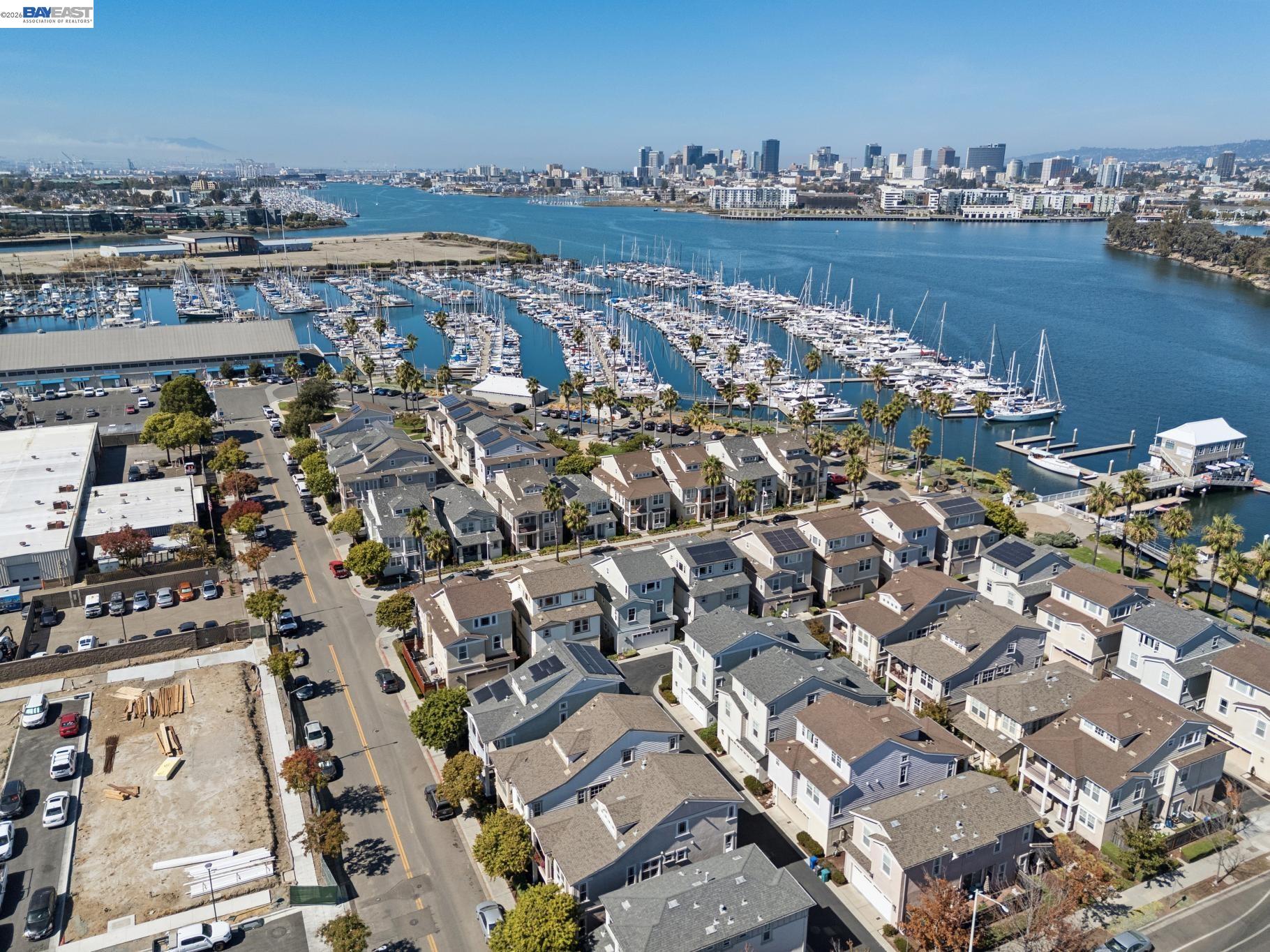 Aerial view of a waterfront neighborhood and boat-filled marina, with a city skyline across the water.
