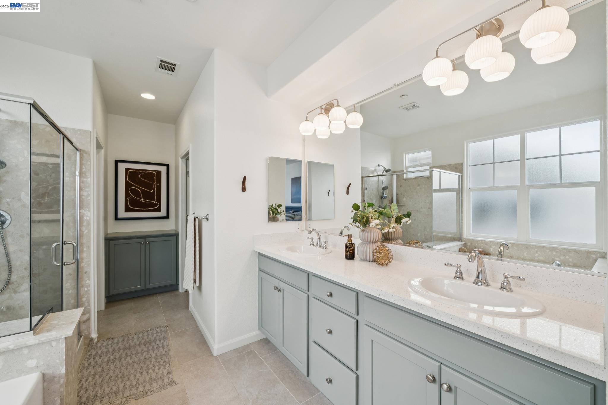 Bright bathroom with a pale gray double vanity, globe pendant lights, and a glass-enclosed shower.