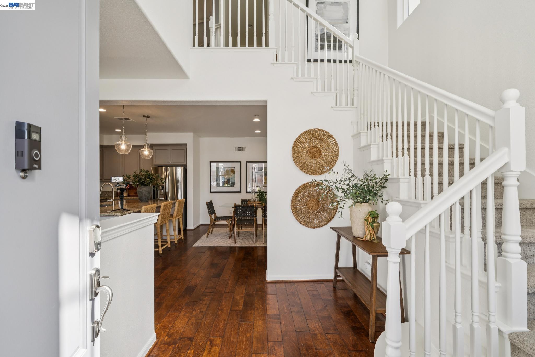 Furnished entry foyer with dark hardwood floors, a white staircase, and an open view of the kitchen and dining area.