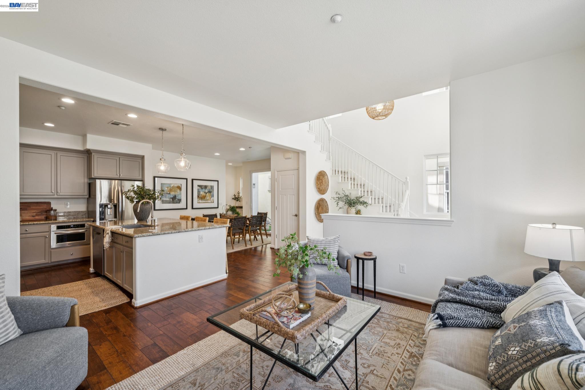 Open-plan living room and kitchen with a granite island, dark wood floors, and a white staircase.