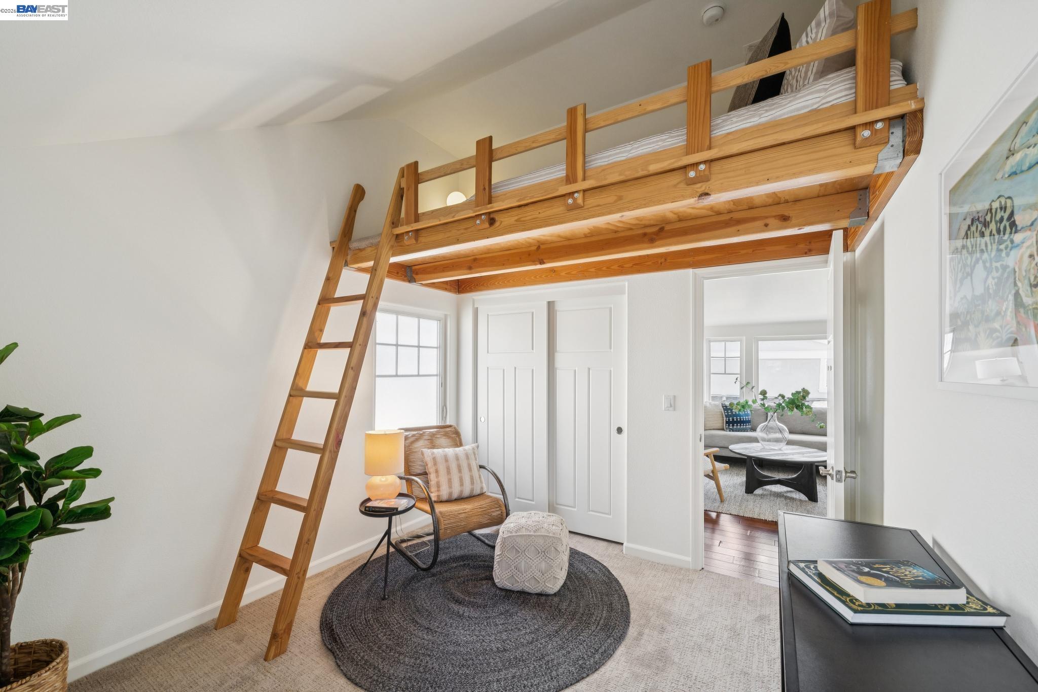 Furnished bedroom with a wooden loft bed, ladder, and sitting area below.