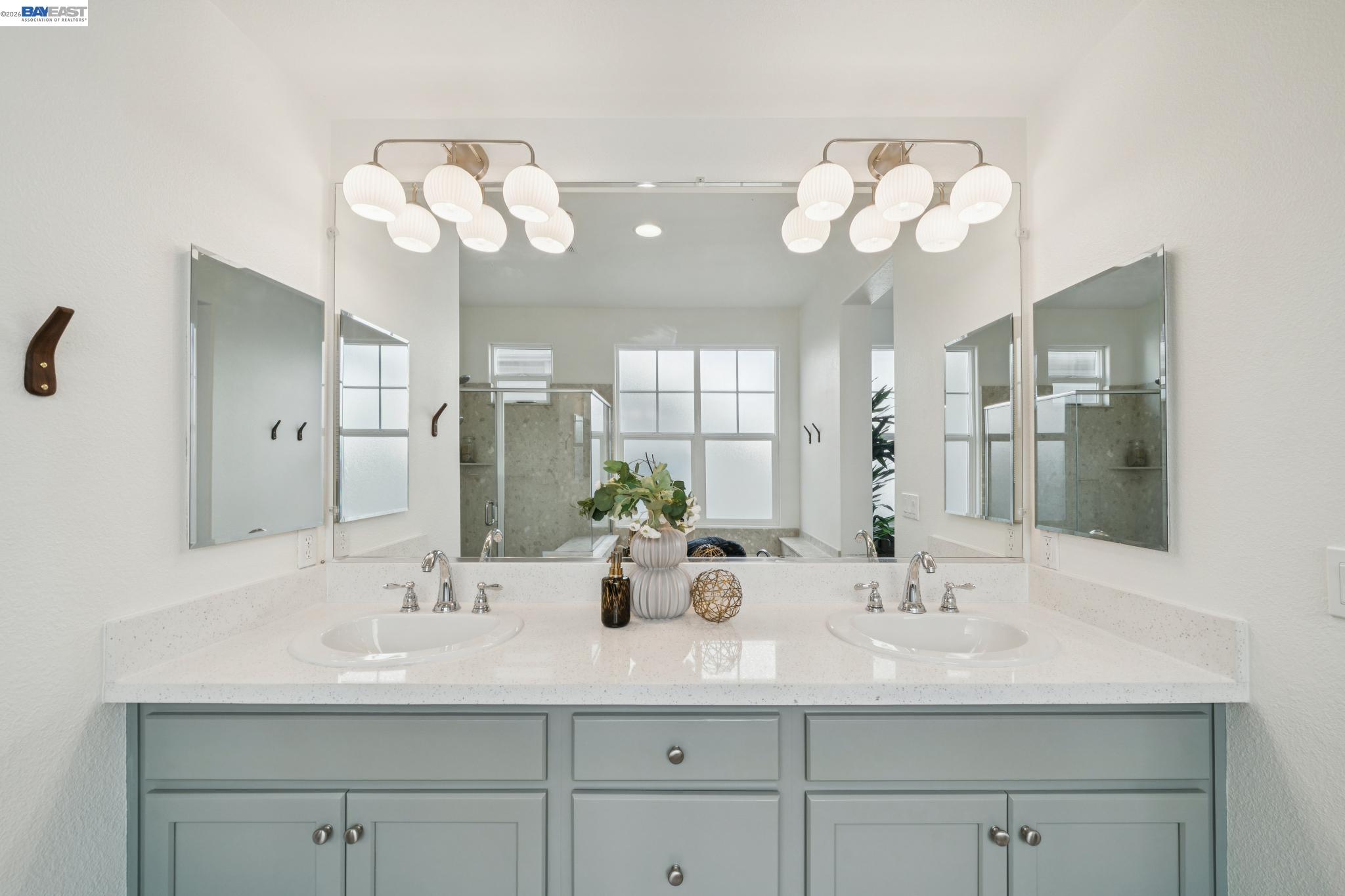 Bathroom double vanity with pale gray cabinets, broad mirrors, and globe lights.