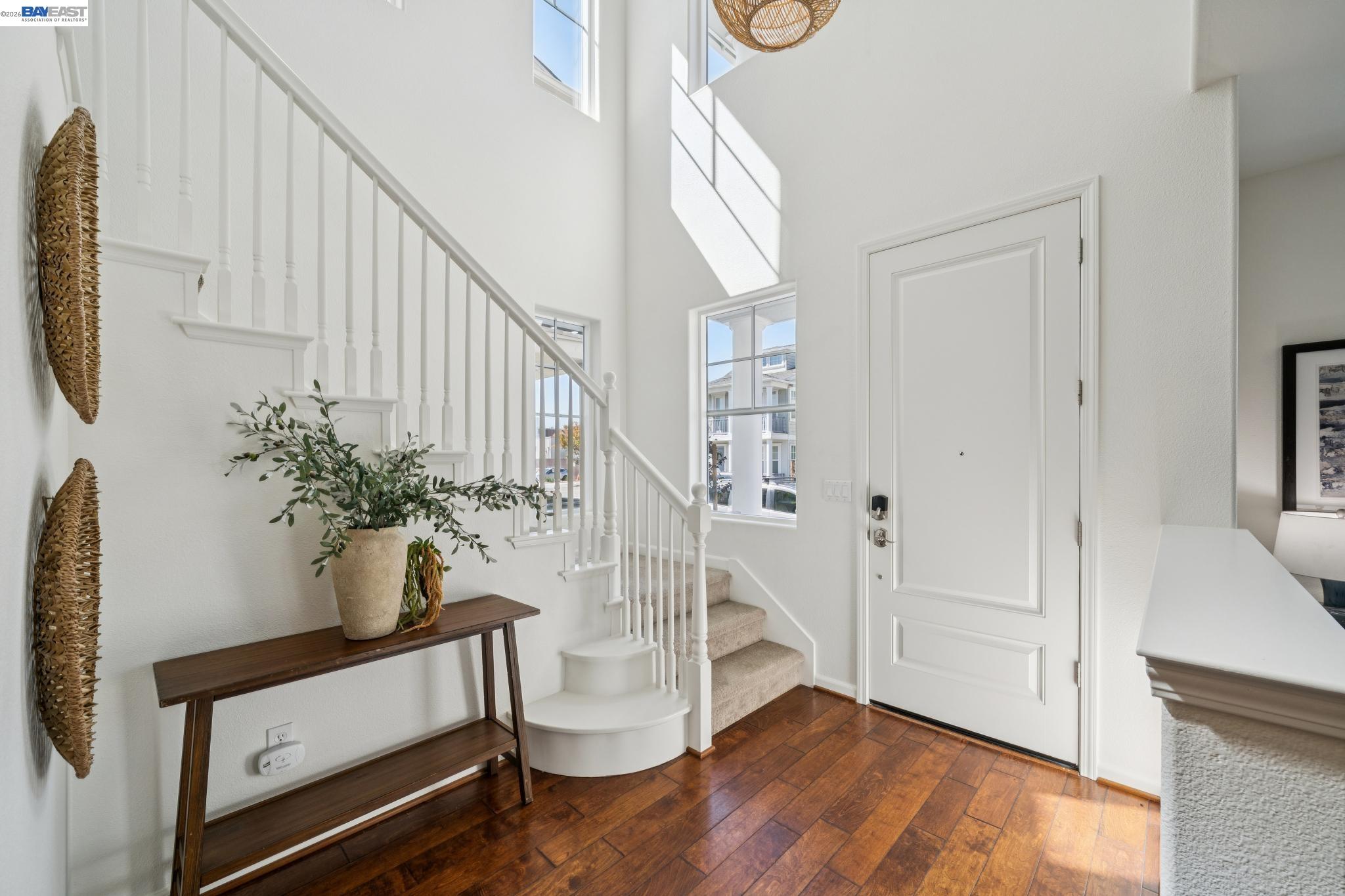 Bright entry foyer with a carpeted staircase, tall windows, and a dark wood console table.