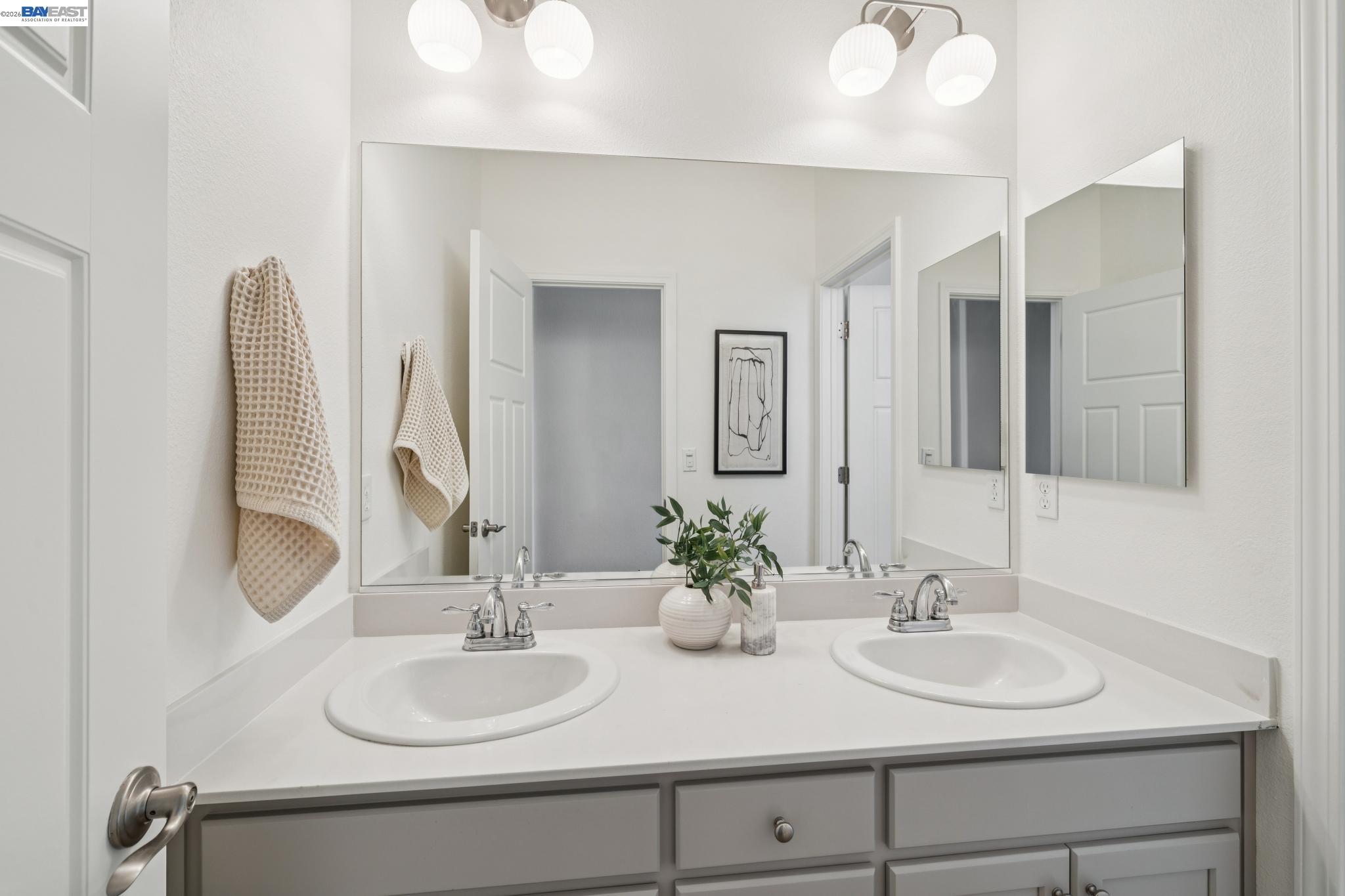 Bathroom with a gray double-sink vanity, broad mirror, and beige towels.