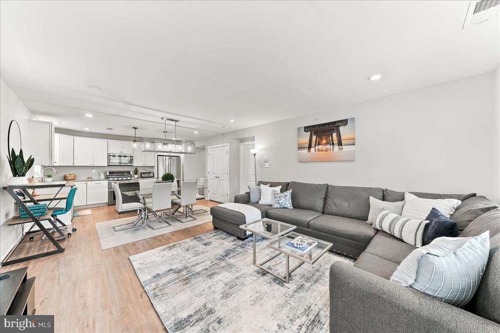 Open-plan living room with a large gray sectional, patterned rug, and white kitchen.