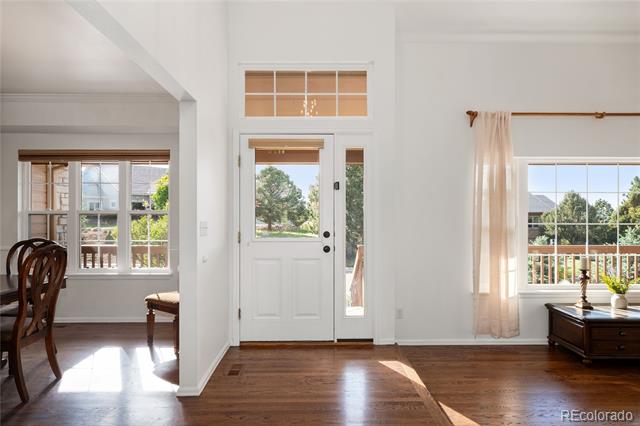 Bright entryway with a white front door, hardwood floors, and windows overlooking a deck.