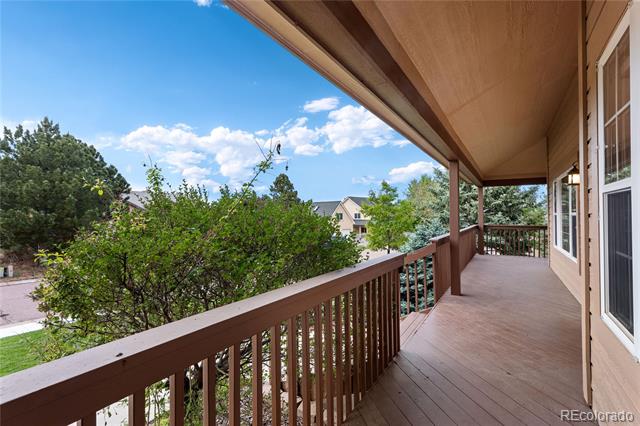 Covered wooden porch with brown railing overlooking trees and neighboring homes.