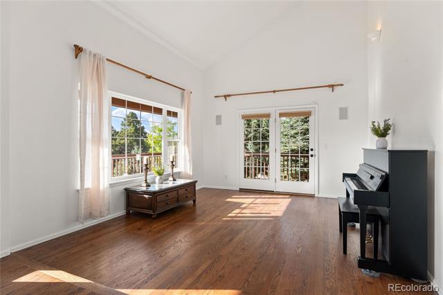 Bright living room with hardwood floors, a black piano, and French doors opening to a deck.
