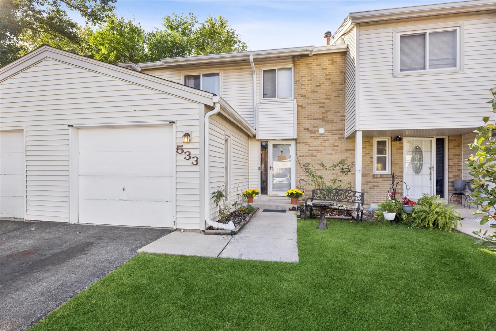 Two-story attached home with cream siding, tan brick, a garage, and a green front lawn.