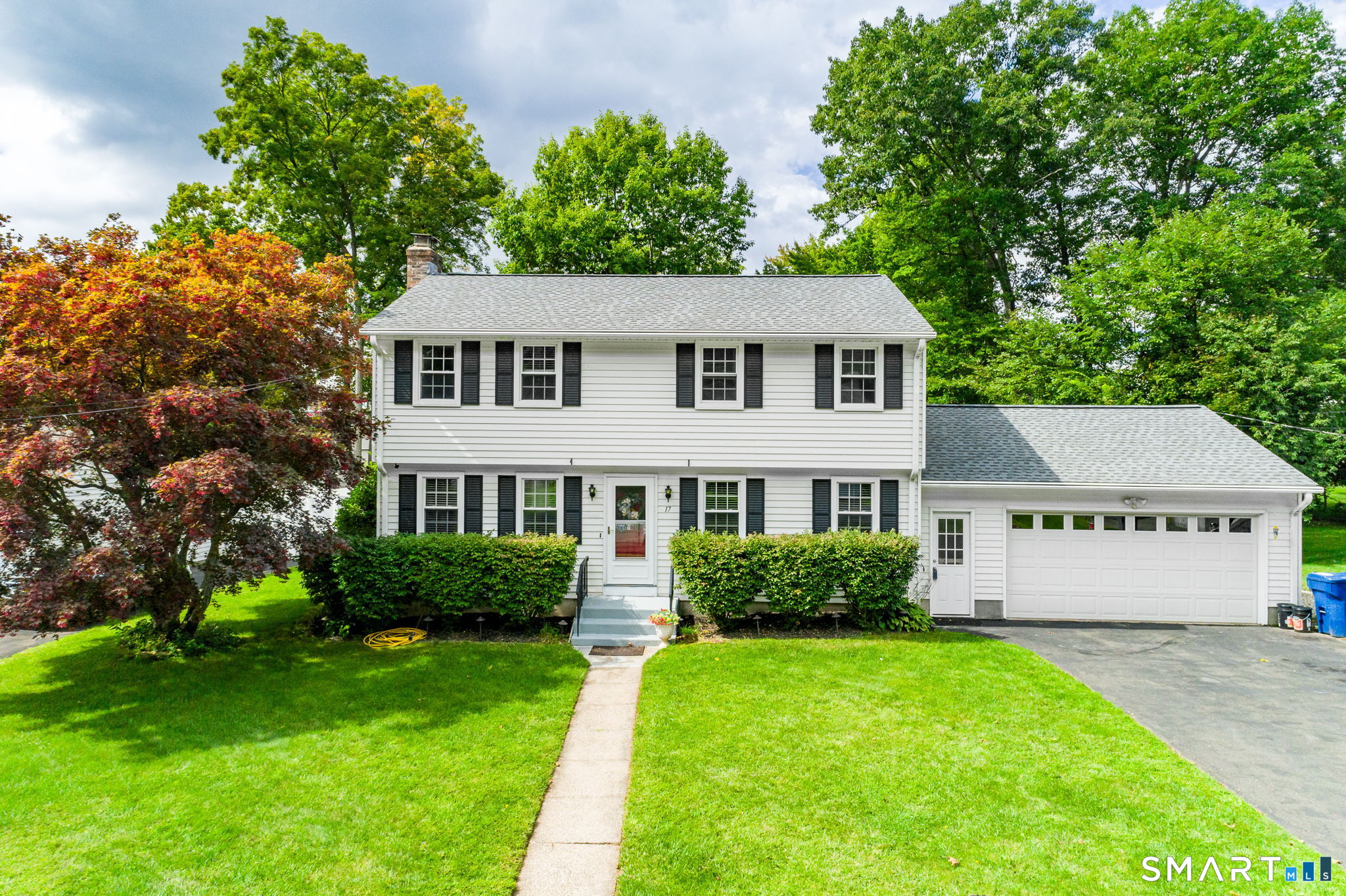 White two-story Colonial home with black shutters, attached garage, and leafy front lawn.
