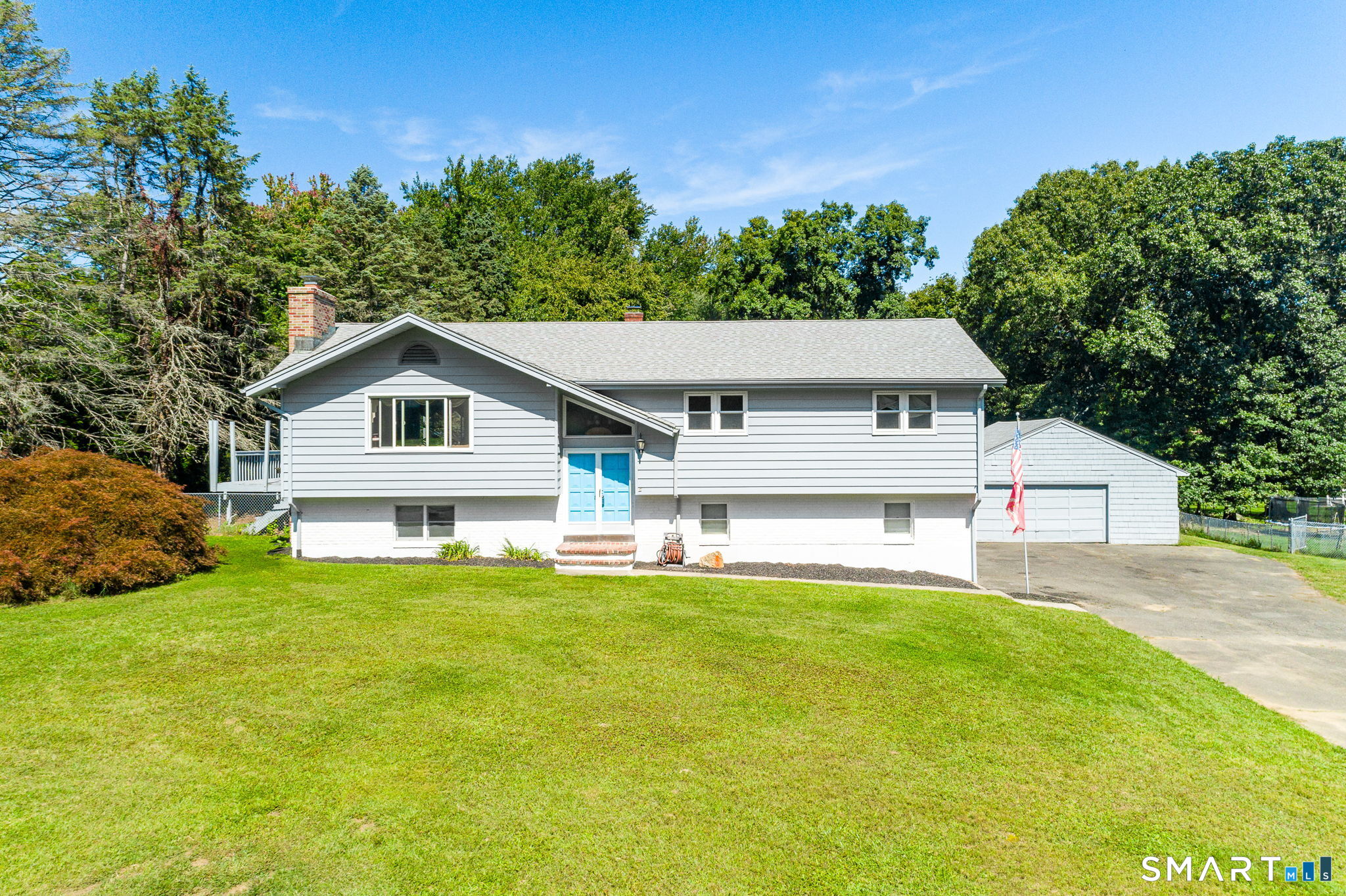 Gray split-level house with bright blue front doors, attached garage, and broad lawn.