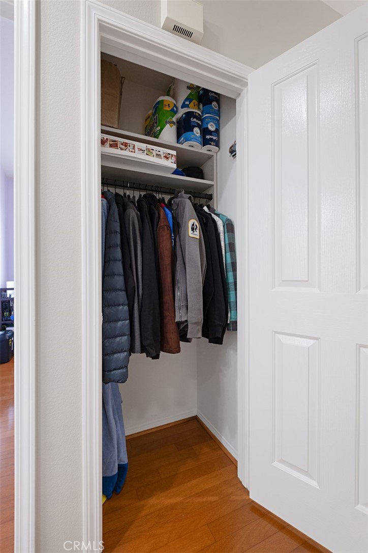 Walk-in closet with coats hanging beneath storage shelves and a white paneled door.