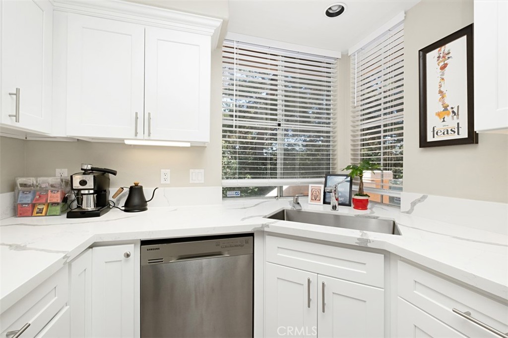White kitchen with veined counters, stainless dishwasher, and corner sink beneath wide windows.