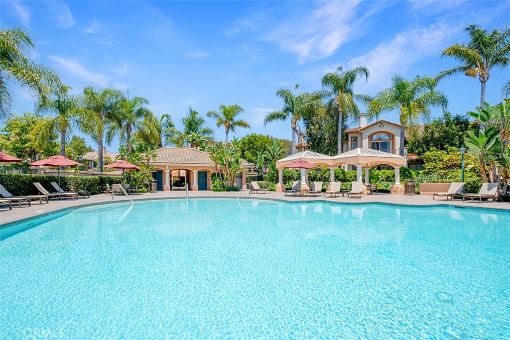 Community pool with turquoise water, palm trees, lounge chairs, and a clubhouse.
