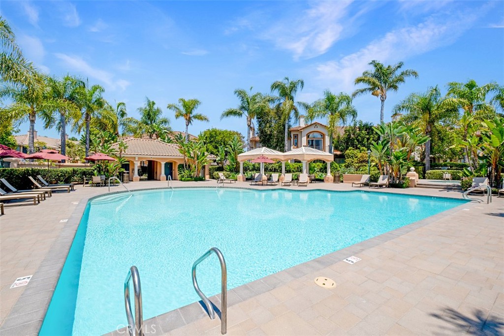 Community swimming pool with turquoise water, palm trees, lounge chairs, and shaded seating.
