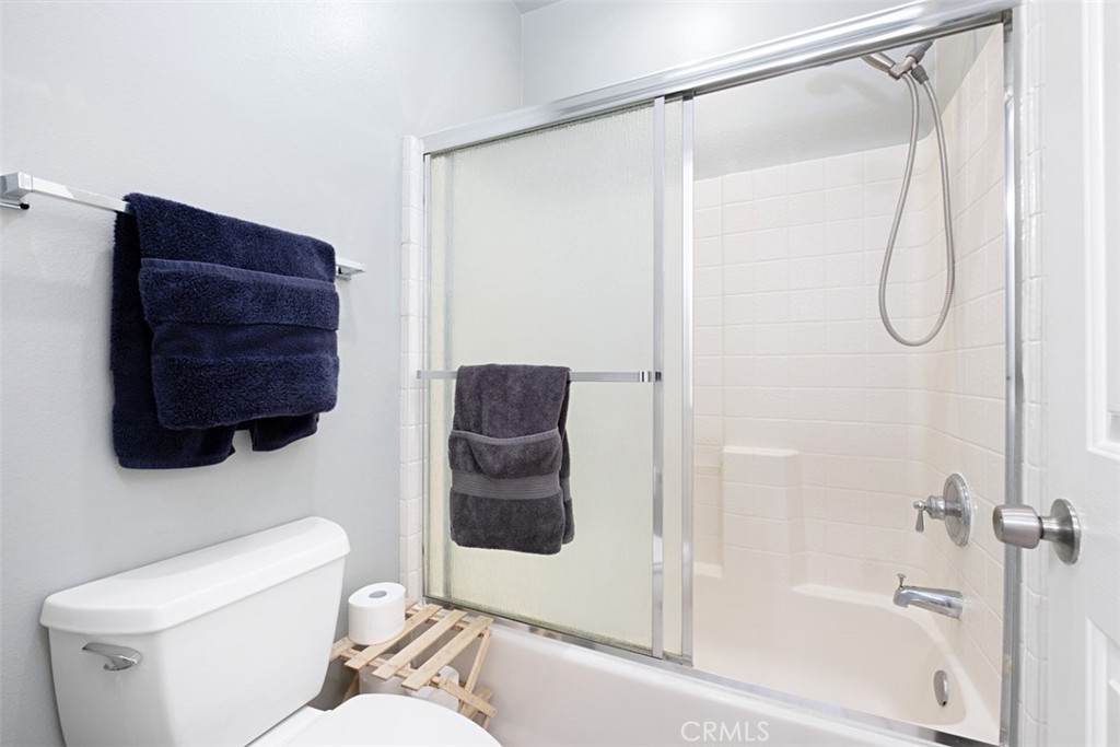 Bathroom with a tub-shower behind frosted glass doors and dark towels hanging nearby.