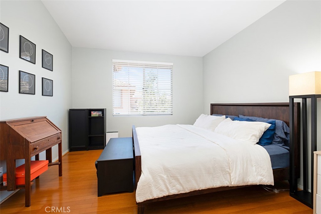 Bedroom with white bedding, blue accent pillows, dark wood furniture, and hardwood floors.