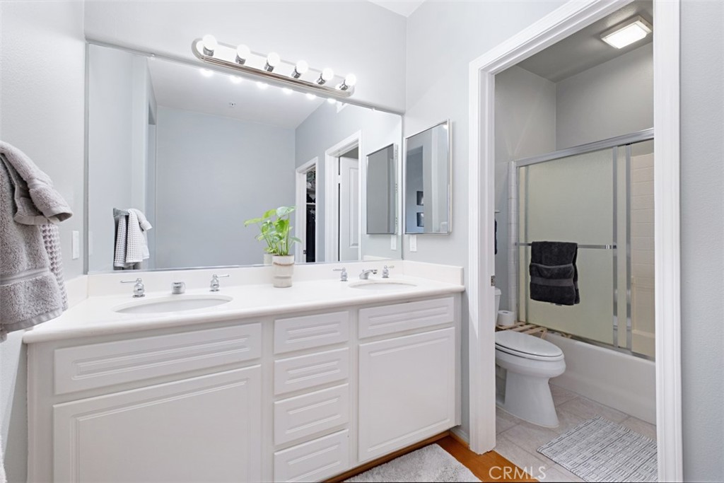 Bathroom with a white double-sink vanity and adjoining tub-shower behind sliding glass doors.