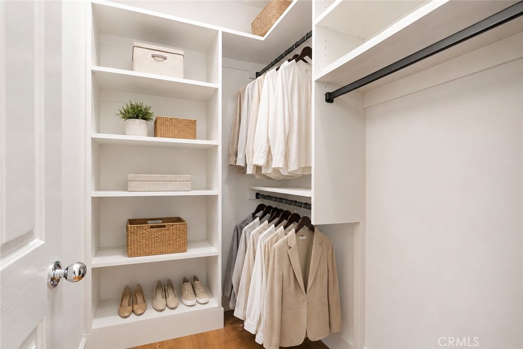 Walk-in closet with white built-in shelves, woven baskets, shoes, and neatly hung neutral clothing.