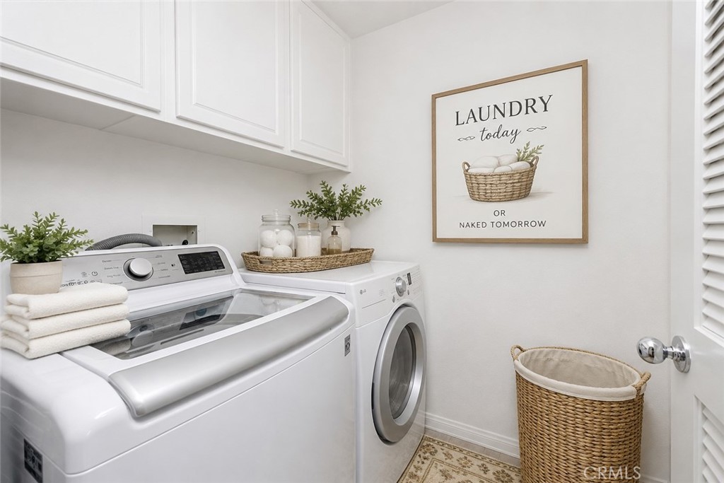 Staged laundry room with white washer and dryer, upper cabinets, and woven baskets.