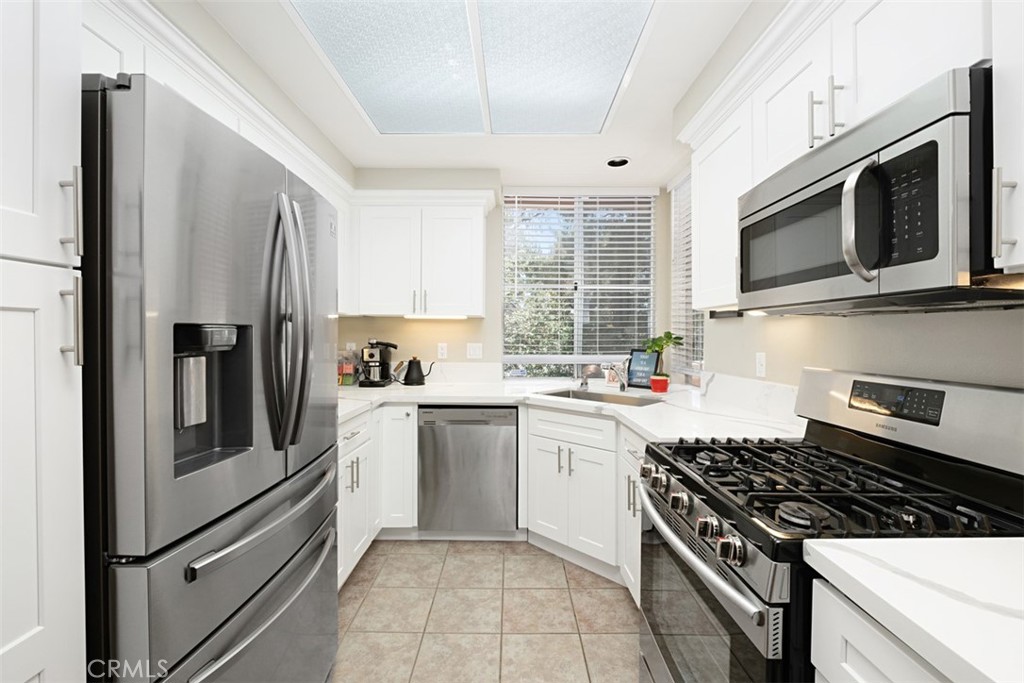 Bright white kitchen with stainless steel appliances, a gas range, and a window above the sink.